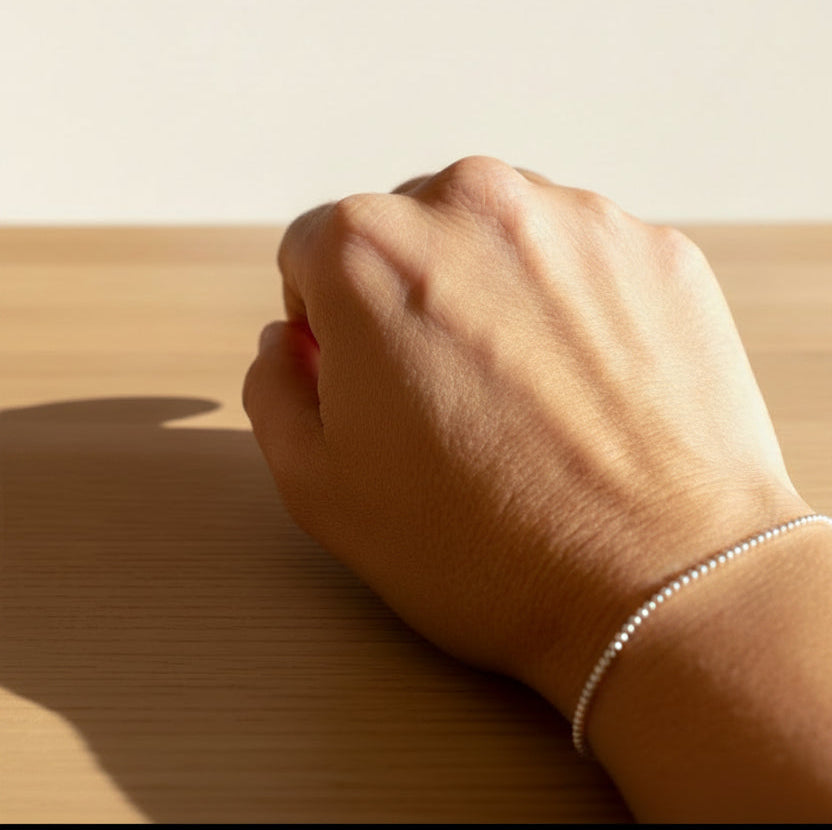 A silver bracelet with mini spheres design, military style,displayed on a person's wrist.